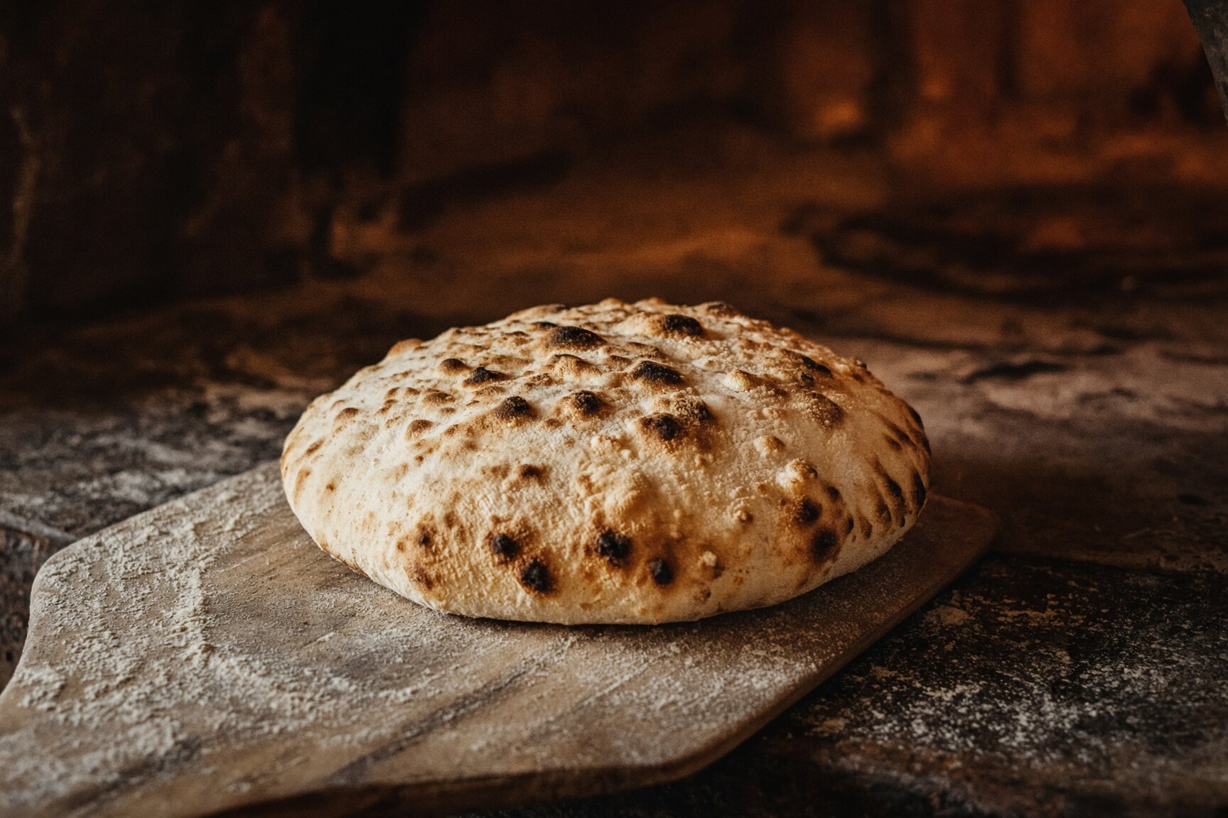 A blistered round of pita on a floured wooden peel in front of the oven mouth — illustrative AI-generated demo image.